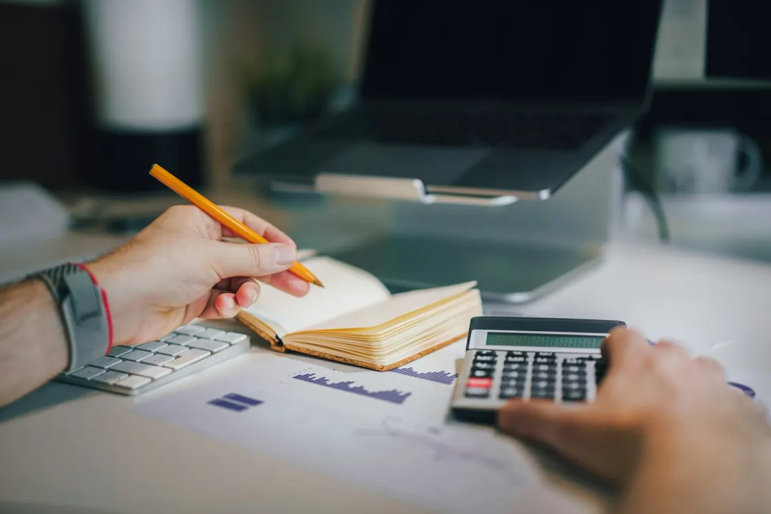 Someone working out figures at a desk with a calculator, a notebook and a printed statement.